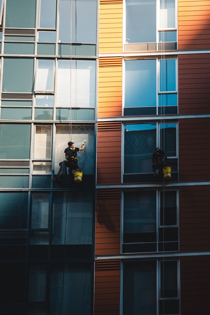 Deux travailleurs suspendus pour laver les vitres d’une façade de gratte-ciel moderne.