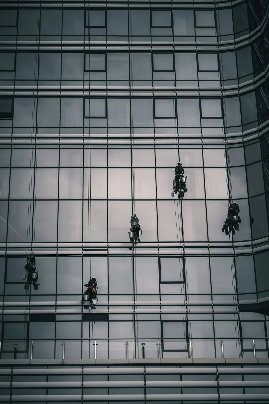 project-01-b Two workers clean windows on a modern glass building facade using a suspended platform.