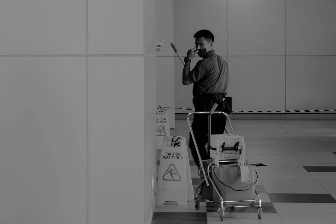 A worker washing high-rise windows while secured by a harness in a city setting.