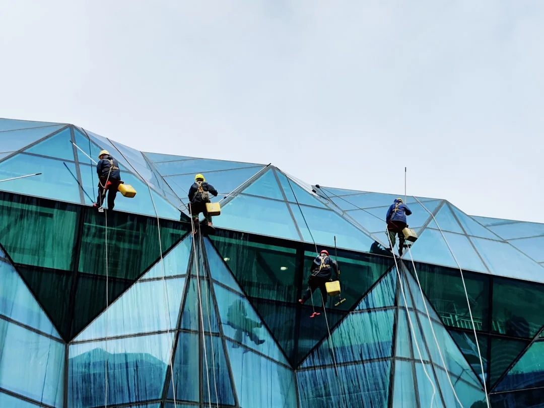 During the day, three rope-suspended window cleaners wash the facade of a modern glass building.